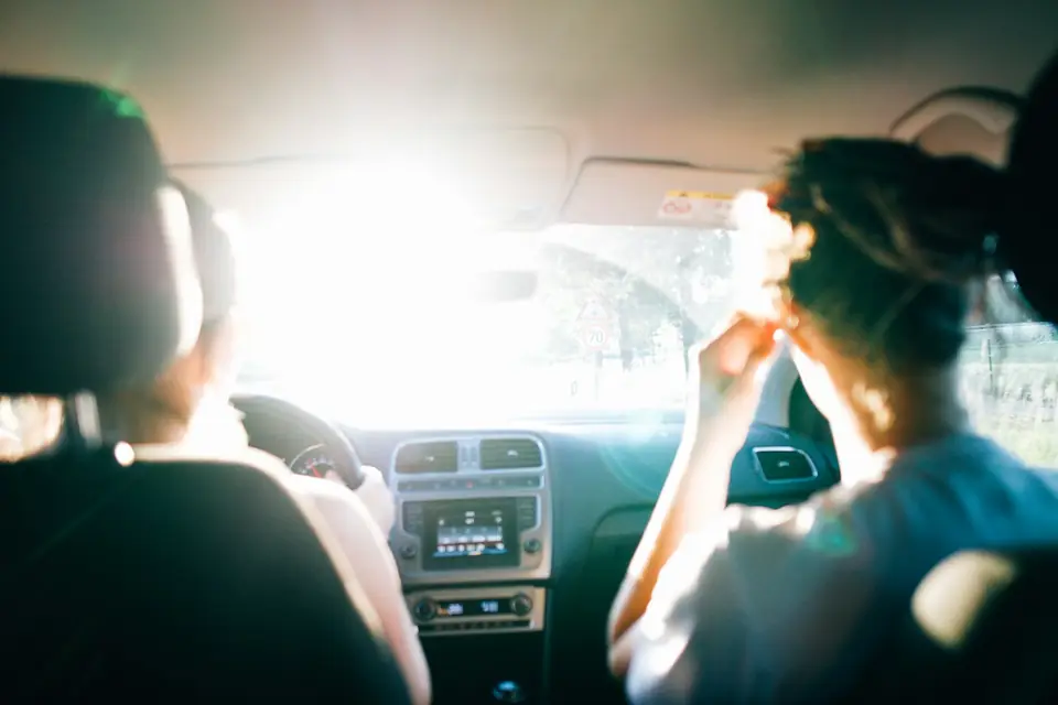 Two friends in a car on a road trip, sun through the windscreen